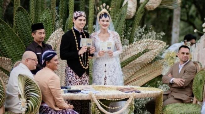 Marriage certificate signed of the happy newly wed Luna Maya and Maxime Bouttier. All decorations are so green, including table and chairs wrapped in leafy green textures, blending seamlessly into the forest backdrop and emphasizing connection with nature [Instagram@/bouttier_maxime/iluminen]